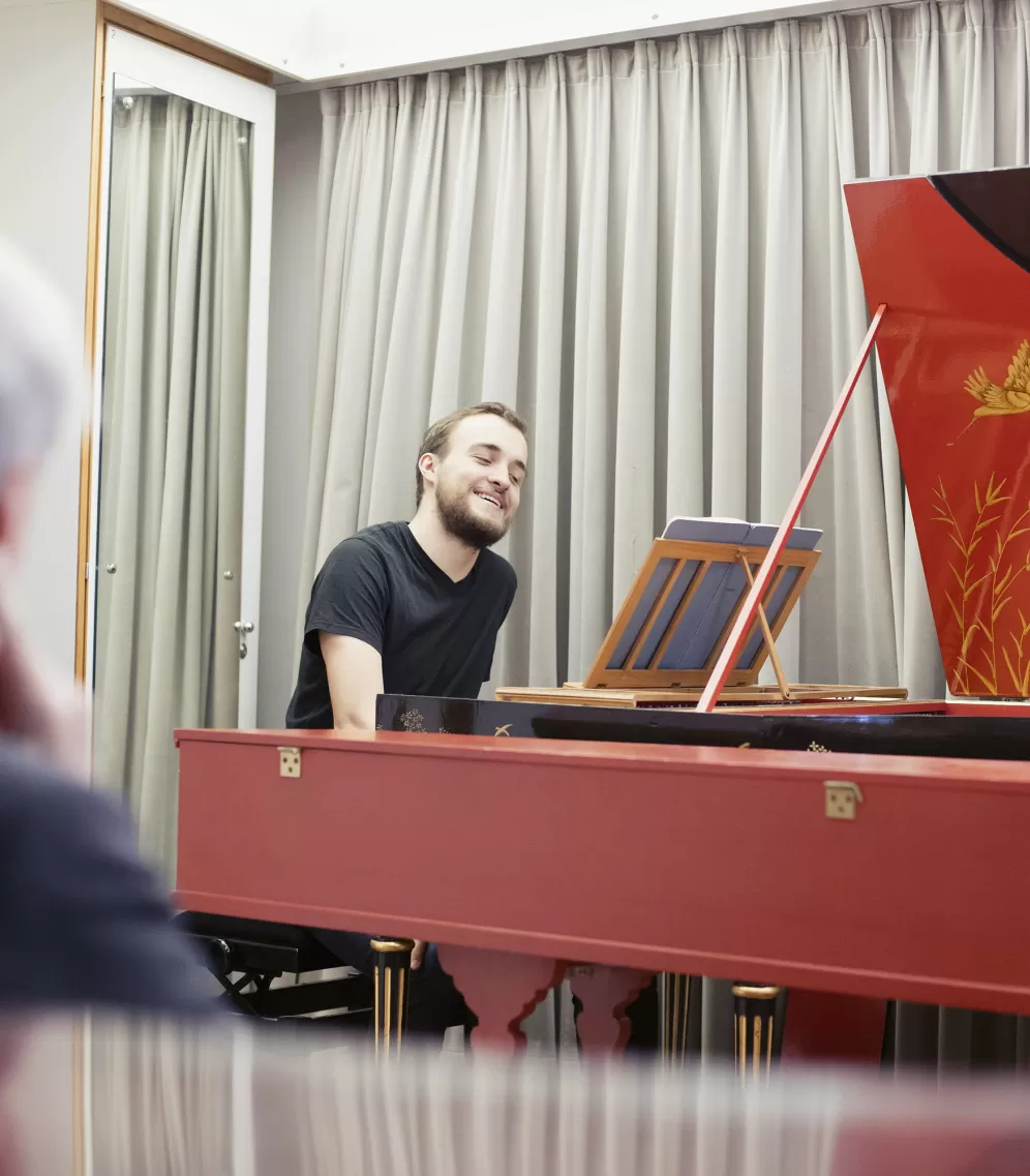 Ein junger Mann sitzt an einem Hammerflügel und lacht.