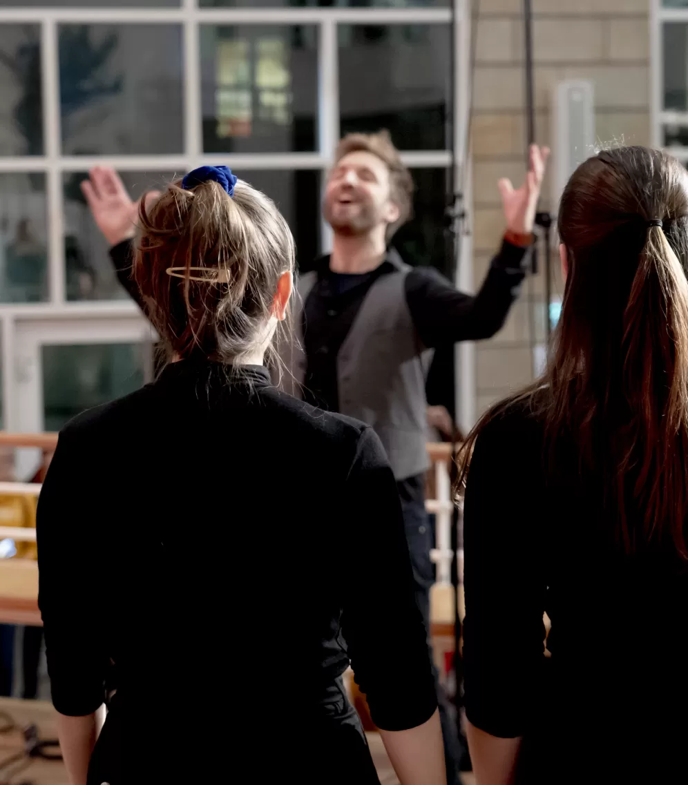 Sängerinnen eines Chores von hinten, vor ihnen der Dirigent