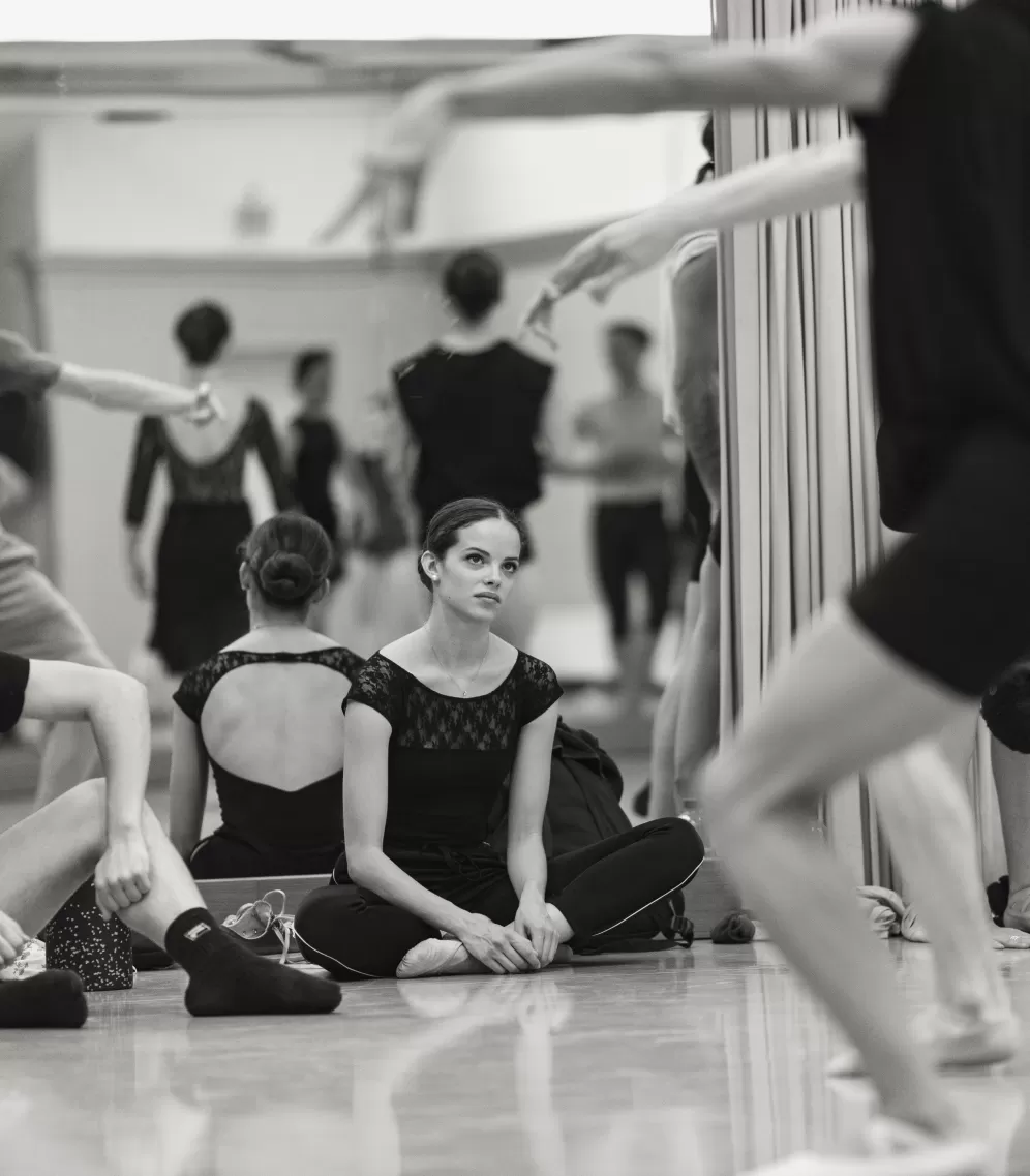 Im Tanzstudio, zwei Tanzstudierende sitzen auf dem Boden und sehen dem Training zu