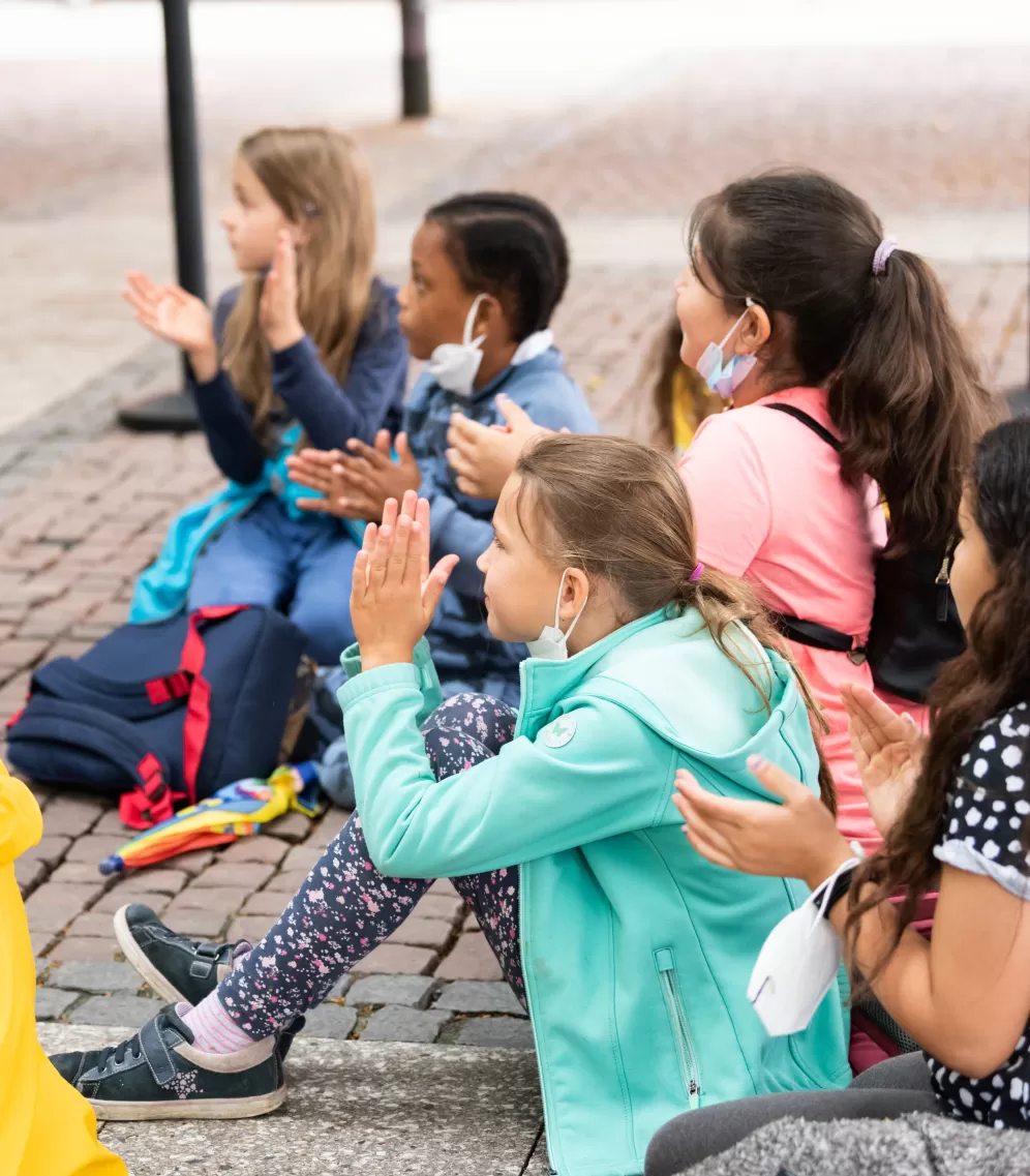 Mehrere Kinder sitzen auf dem Boden und applaudieren
