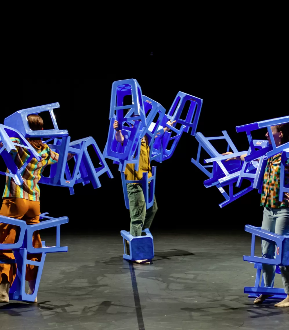 Szene beim Tanzmarathon 2021, drei Personen tragen viele blaue Hocker an ihren Körpern und bewegen sich auf der Bühne.