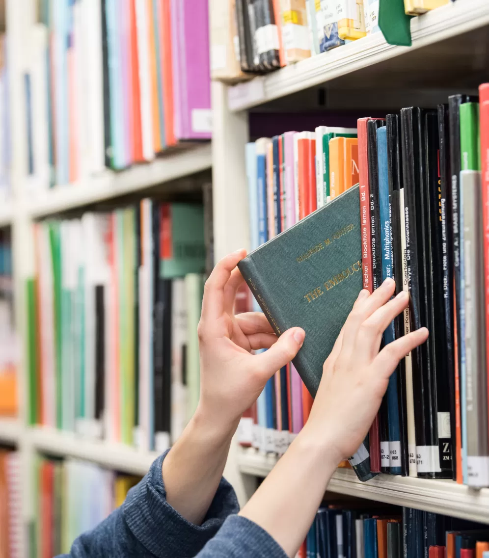 Hände, die ein Buch aus dem Regal nehmen