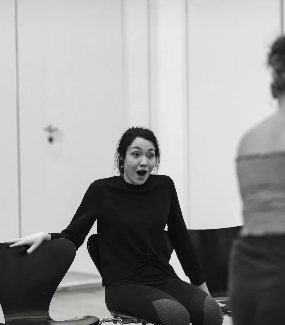 Eine singende Studentin sitzt auf einem Stuhl in einer Stuhlreihe