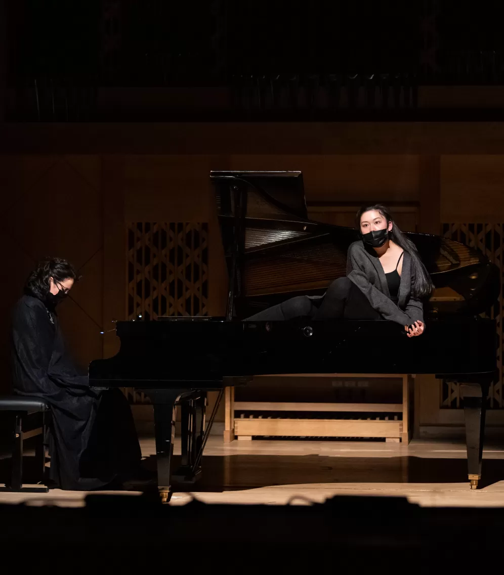 Ein Flügel, der mit einem Scheinwerfer von oben beleutet ist. Eine Person sitzt auf dem Klavierstuhl, die andere sitzt im geöffneten Flügel. Beide sind schwarz gekleidet.