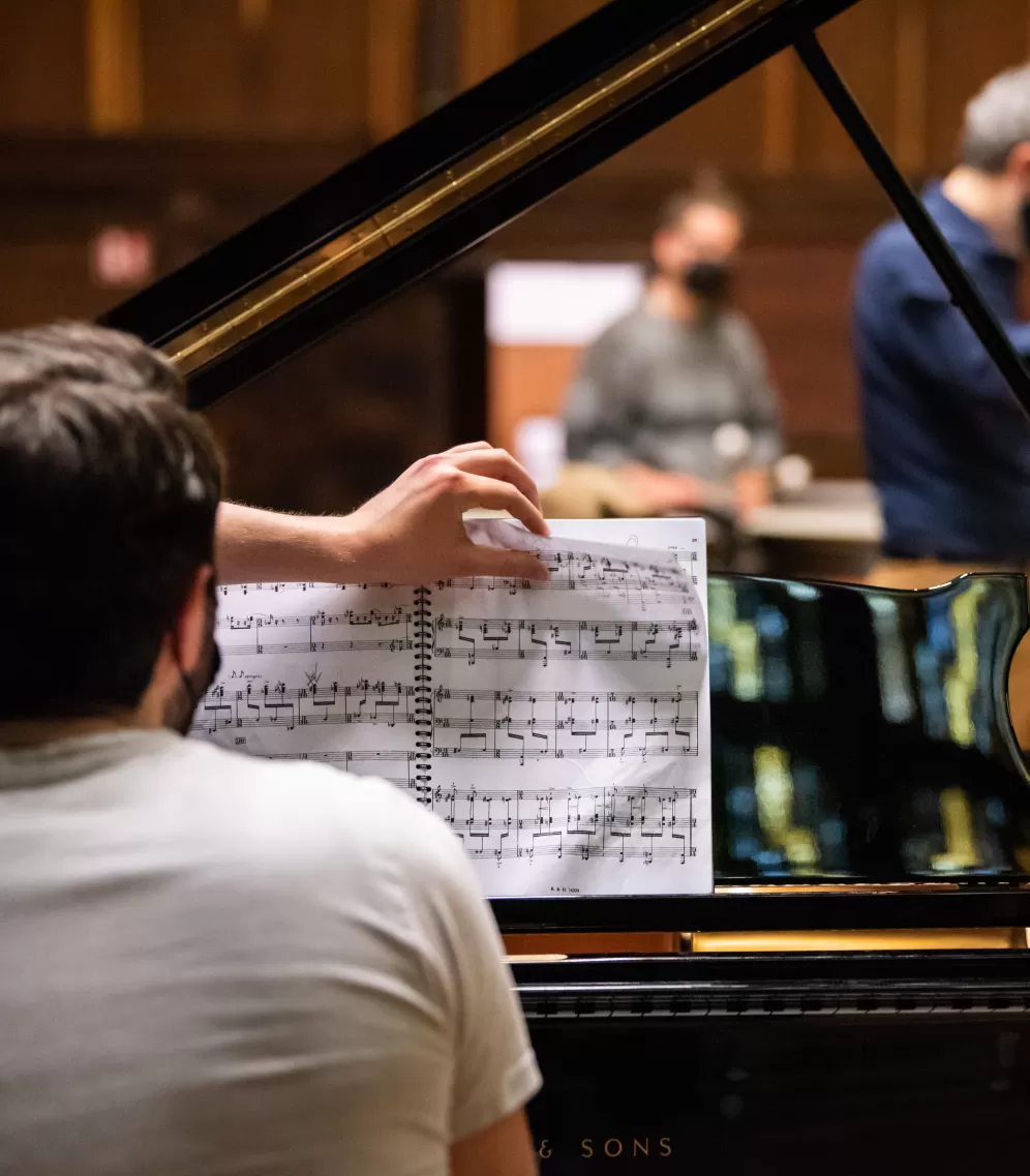 Ein Pianist sitzt am Flügel während eine andere Hand die Noten umblättert