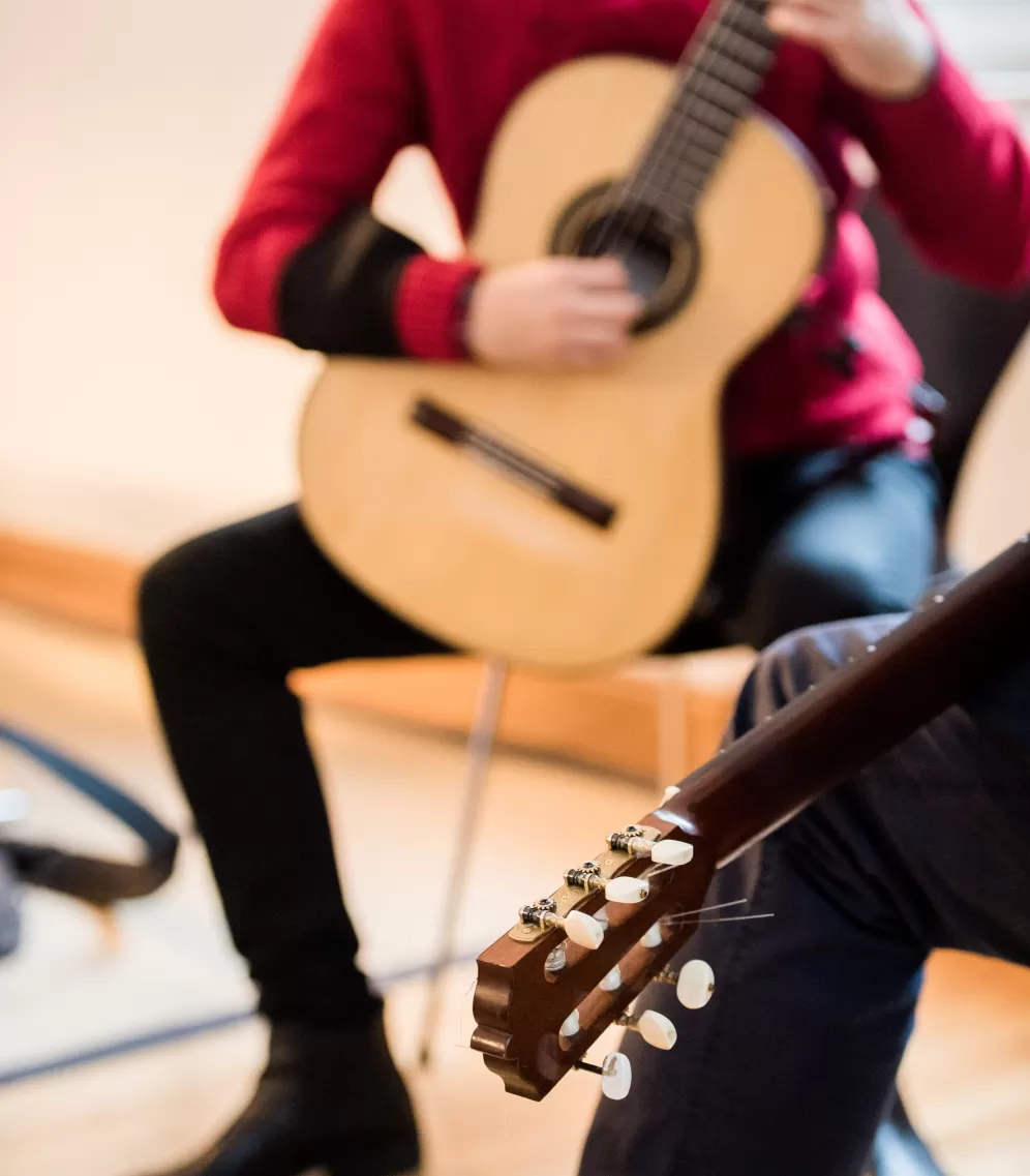 Unterricht im Fach Gitarre, im Vordergrund die Gitarre des Dozenten, im Hintergrund spielt der Student.