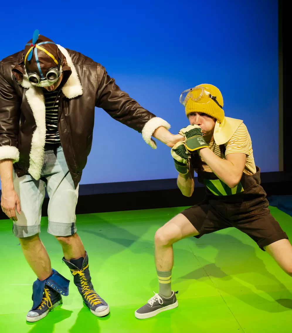 Schauspieler pustet in die Finger einer zweiten Schauspielers, der vorgibt, dadurch aufgepumt zu werden.