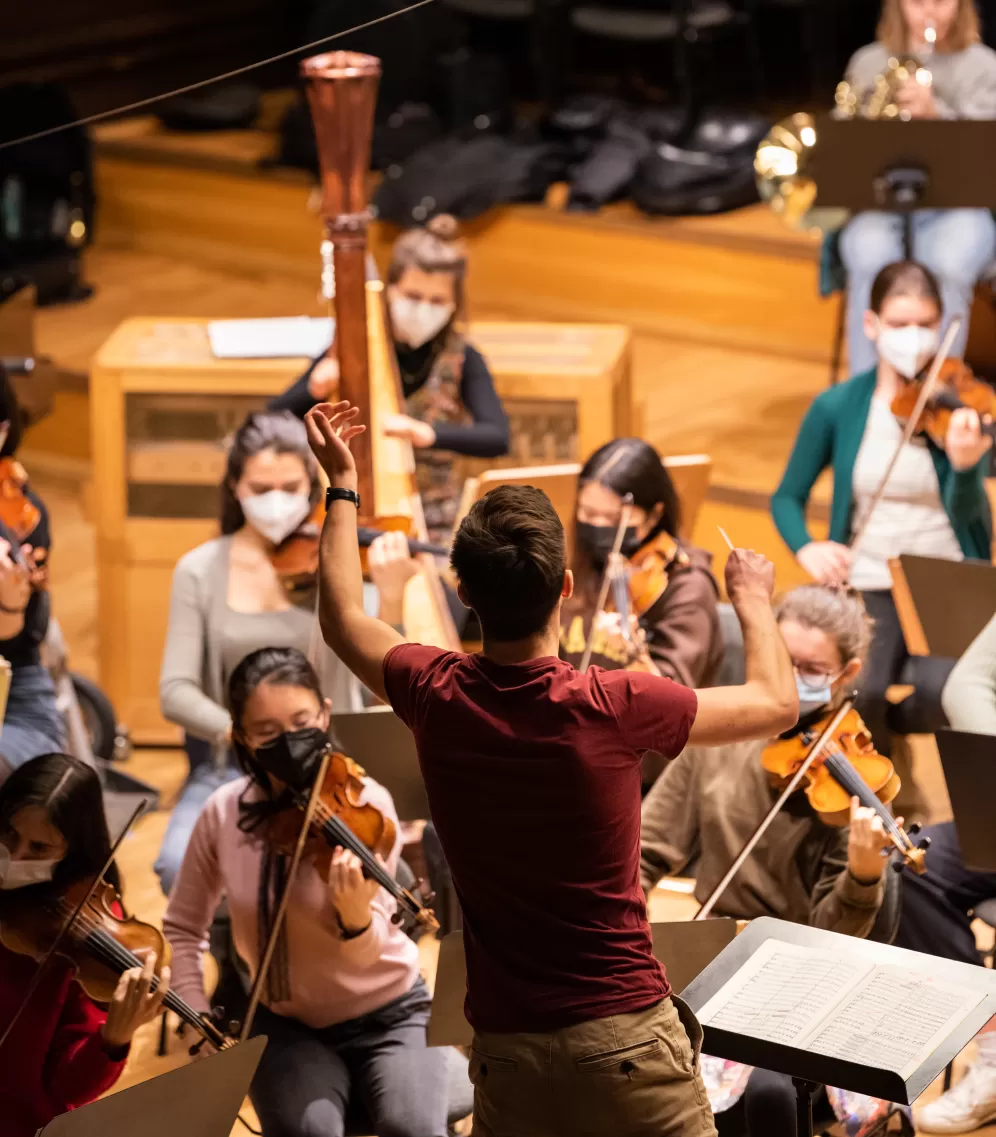 Dirigierstudent leitet ein Orchester, Hand und Taktstock erhoben.