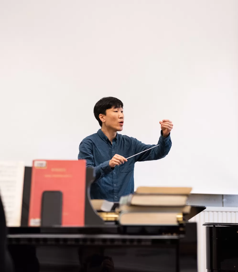 Dirigierstudent im Unterricht an der HfMDK Frankfurt, im Vordergrund ein Pianist am Klavier.