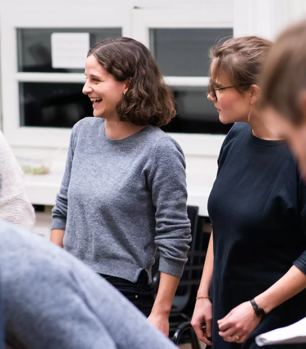 Zwei Studentinnen in einer Probe des Pop- und Jazzchors, eine der beiden lacht.