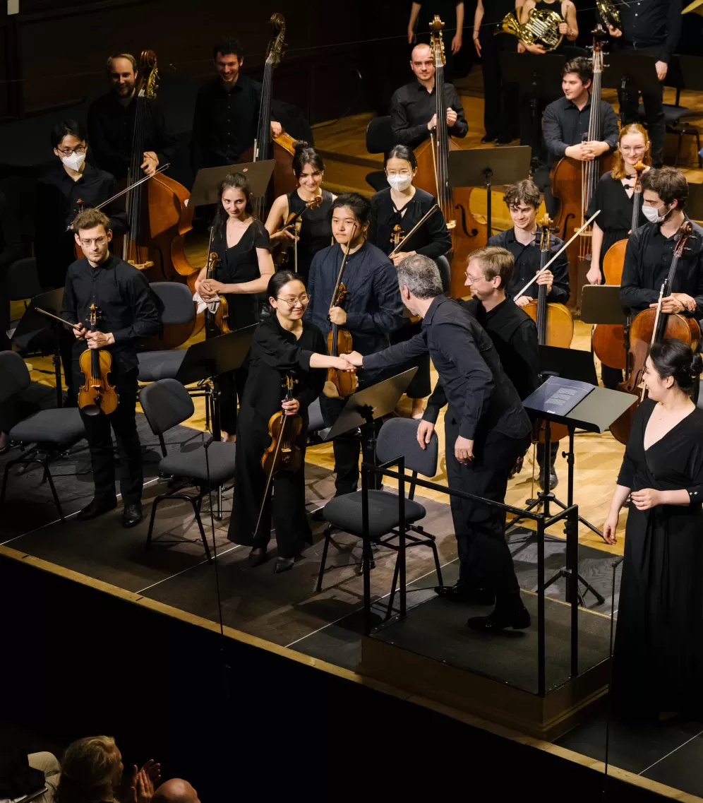 Der Dirigent schüttelt der Konzertmeisterin nach einem Konzert von Chor und Orchester auf der Bühne des Großen Saals die Hand.