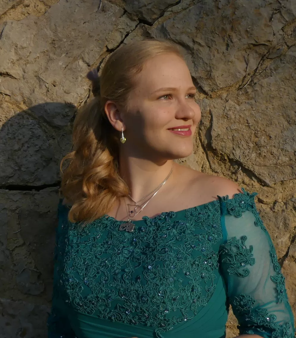 Johanna steht in einem Ballkleid vor einer Bruchsteinmauer und sieht in die Abendsonne.