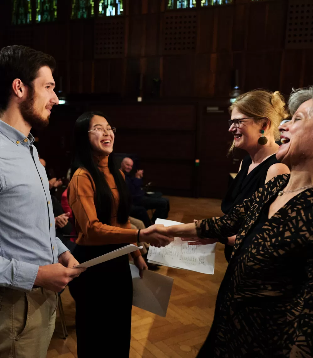 Vier Personen stehen sich gegenüber und lachen. Zwei schütteln sich die Hand. Im Hintergrund sitzt klatschendes Publikum.