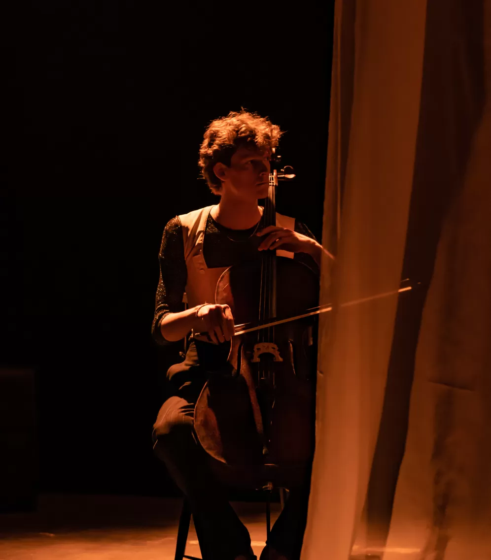 Cellist auf Theaterbühne, Blick nach rechts, transparenter Vorhang auf der rechten Seite