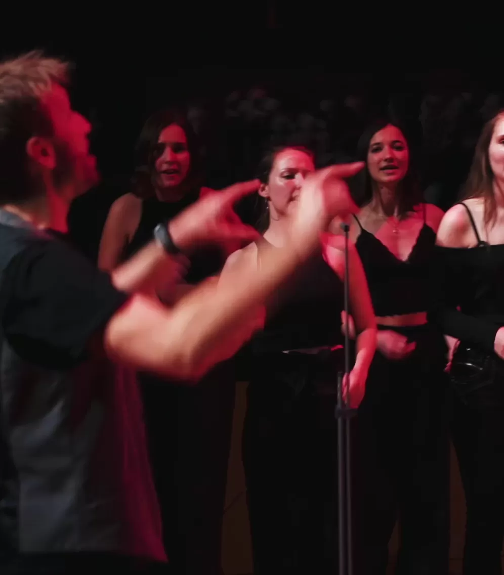 Sängerinnen des HfMDK Pop- und Jazzchors während eines Konzerts, im Vordergrund Chorleiter Prof. Fabian Sennholz.