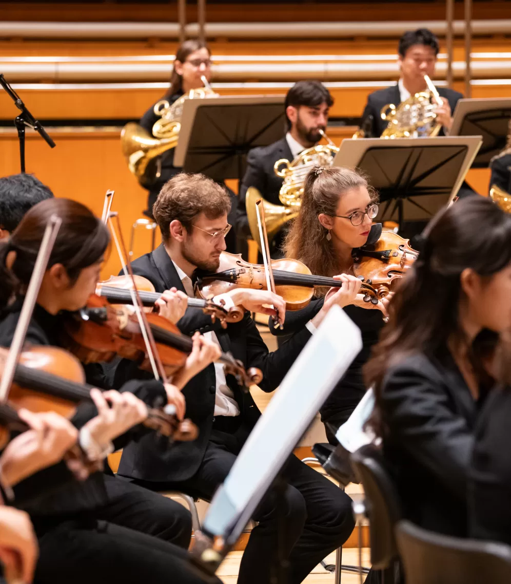 Mehrere Musiker*innen spielen Geige beim Orchesterkonzert im hr-Sendesaal, dahinter spielen vier Studierende Horn