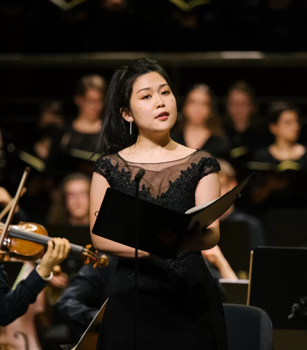 Solo-Sängerin in schwarzem Kleid mit dem HfMDK-Orchester auf der Bühne im Großen Saal