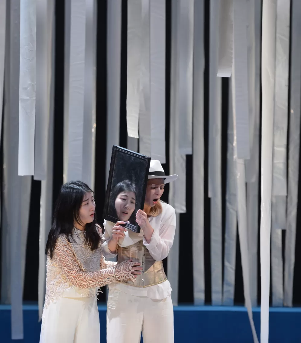 Zwei Musiktheaterdarsteller*innen mit einem Spiegel zwischen ihnen auf der Bühne.