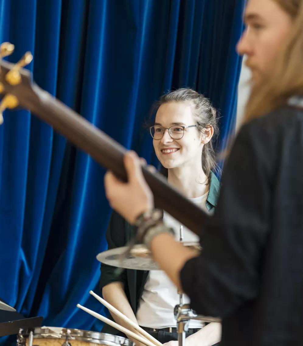 Ein lächelnder Schlagzeuger im Band-Coaching. Vorne rechts ist unscharf der Bassist zu sehen.