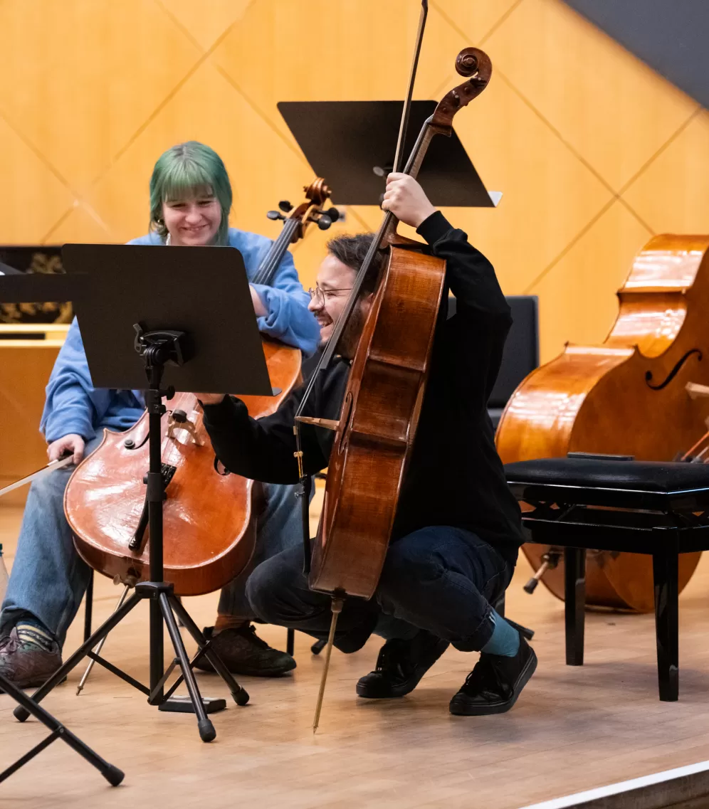 Eine Cellistin und ein Cellist lachen gemeinsam während einer Probe im Kleinen Saal