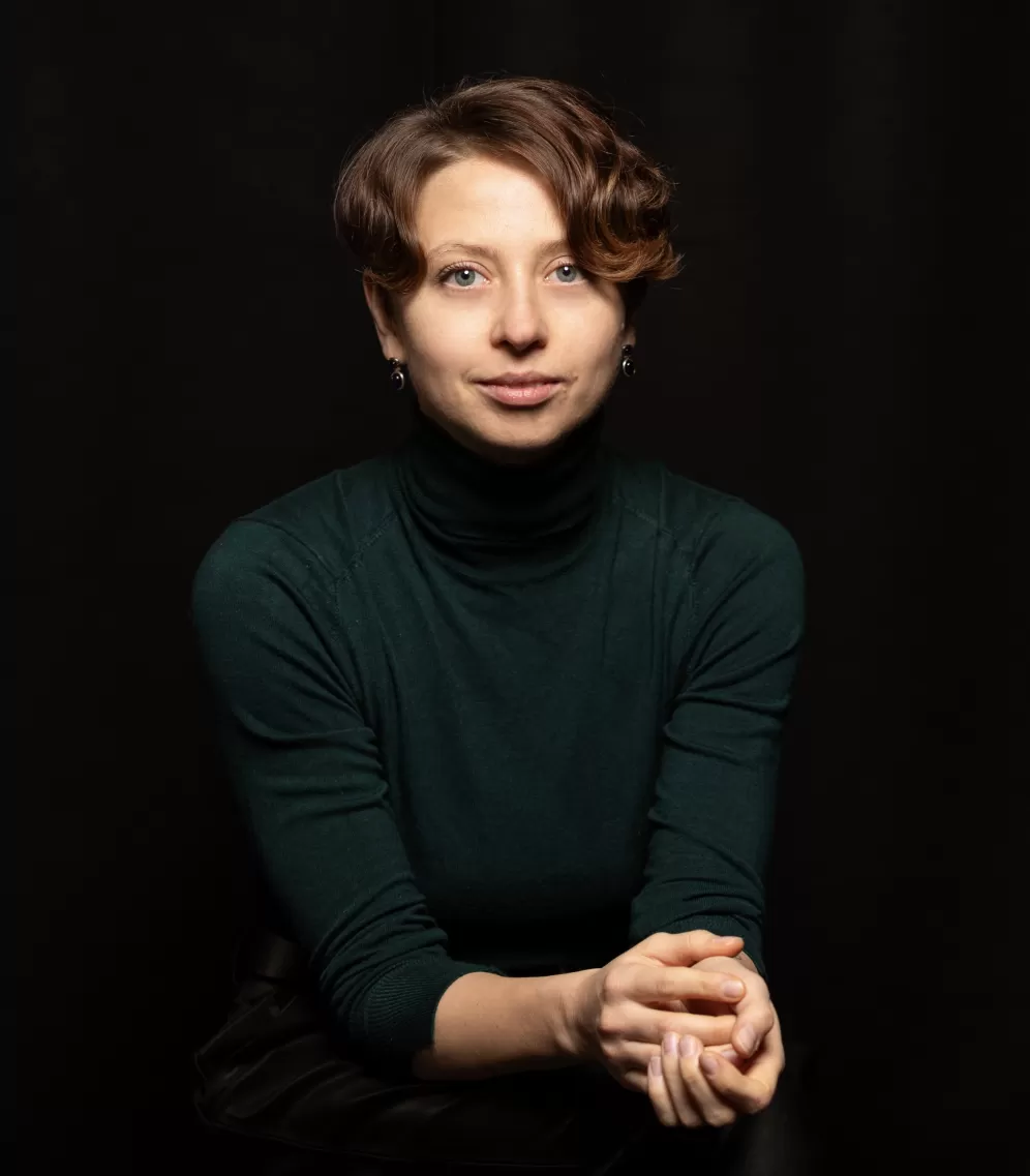 a person sitting with her hands together and looking at the camera