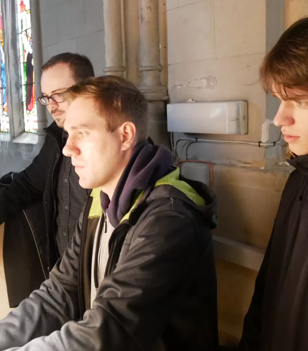 Ein Student spielt an einer Orgel, zwei Personen schauen zu