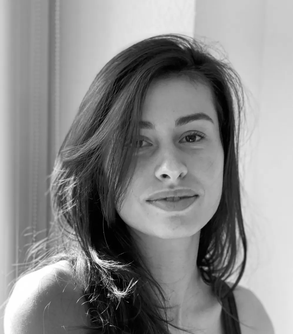 Das Bild zeigt eine junge Frau mit langen, dunklen Haaren und neutralem Gesichtsausdruck in Schwarz-Weiß.