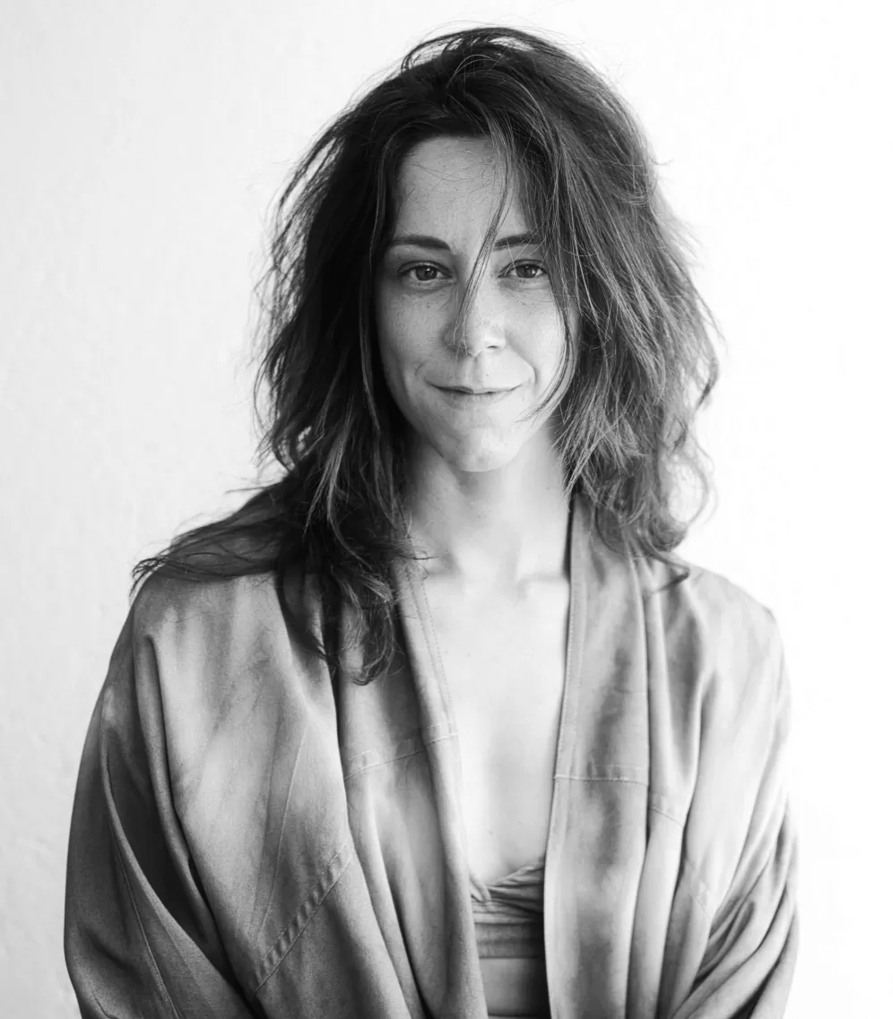 black& white profile picture of a 35 year-old mediterranean woman with messy hair and a vest