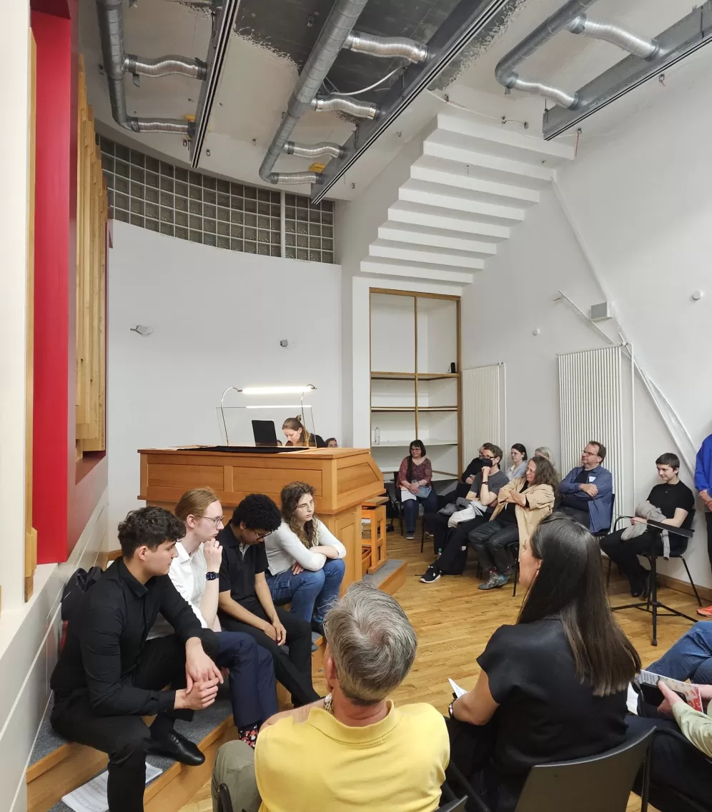 Blick in den Raum während des Konzerts. Menschen sitzen auf Stühlen und dem Boden und schauen der Organistin zu.