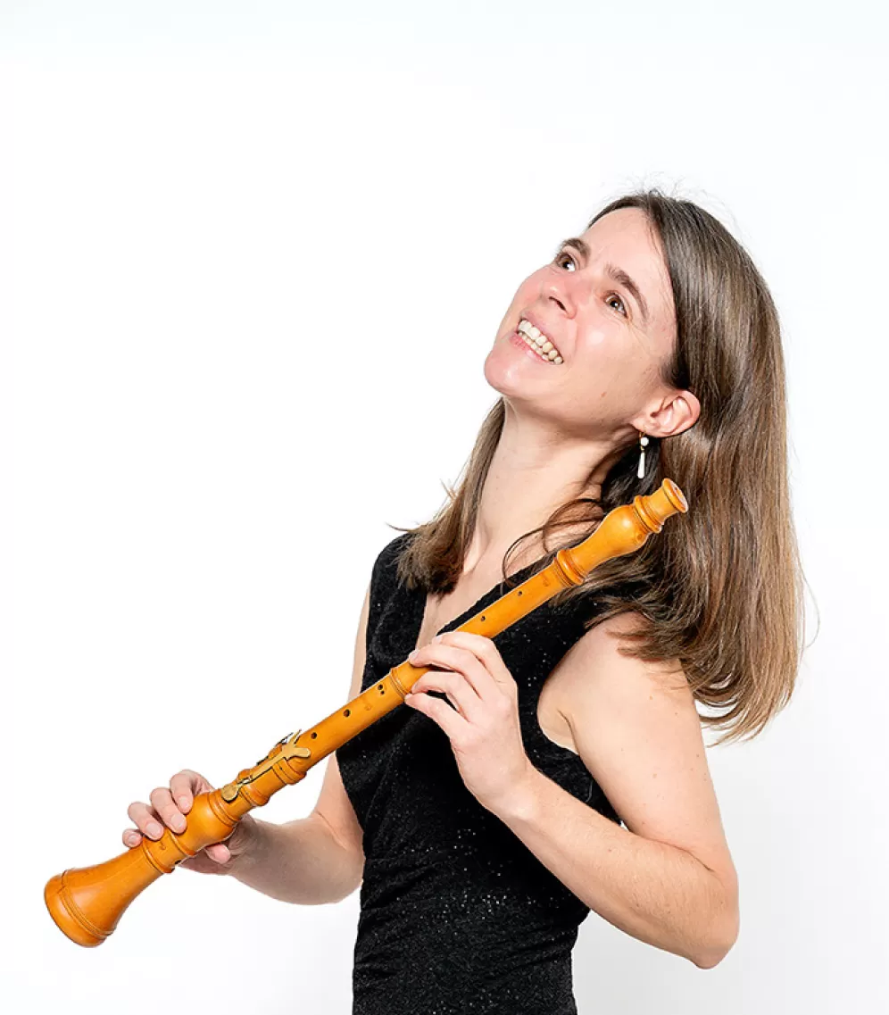 Eine Frau in einem schwarzen Kleid hält lächelnd eine historische Oboe in der Hand.