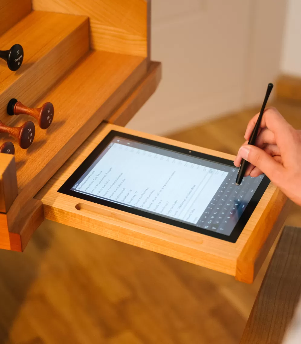 Hand einer Person, die auf dem in den Spieltisch der Rieger-Orgel integrierten Tablet etwas eingibt.