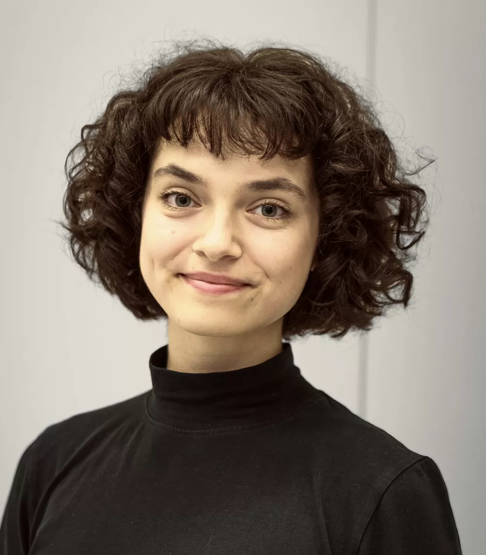 A person with short curly hair wearing a black shirt, smiling into the camera