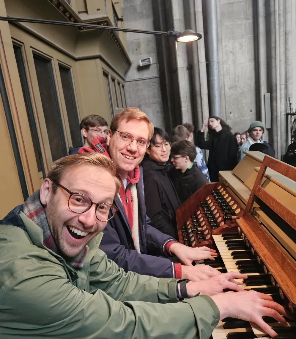 Zwei Studenten sitzen gemeinsam an der Orgel der Votivkirche und lachen in die Kamera