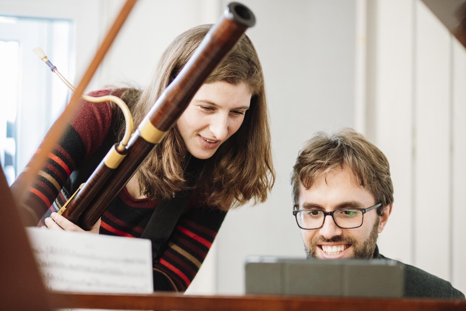 Eine junge Frau mit Fagott und ein junger Mann am Cembalo, beide lächeln.