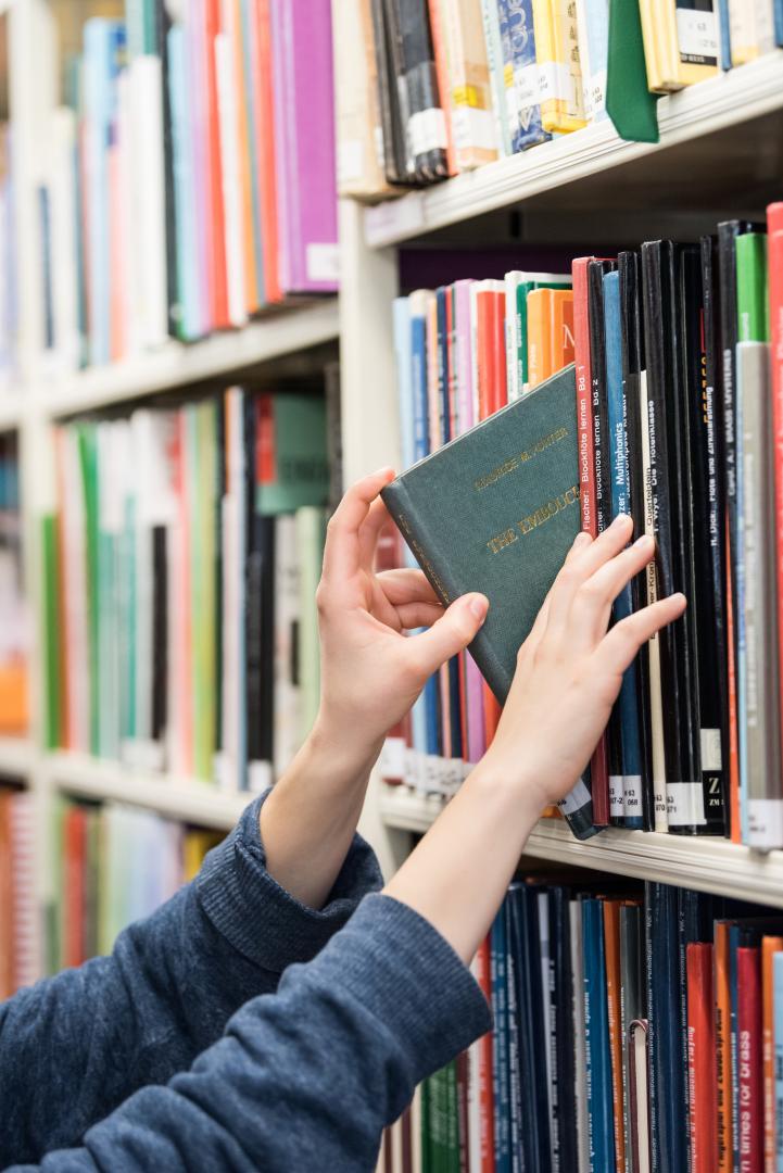 Eine Person zieht ein Buch aus einem Bücherregal.