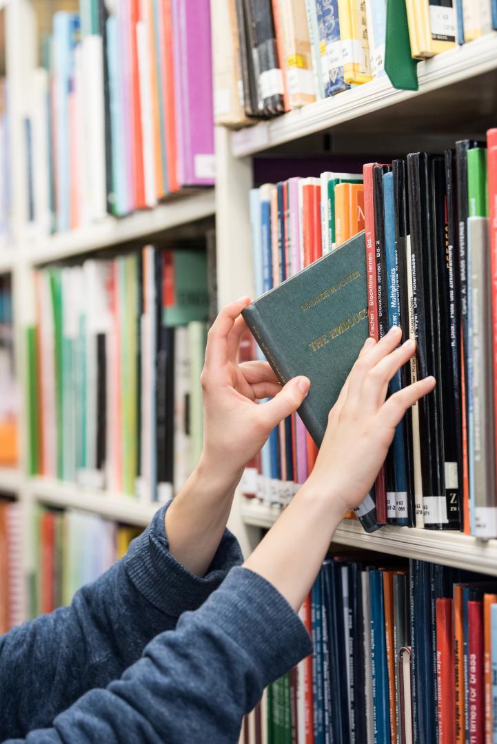 Eine Person zieht ein Buch aus einem Bücherregal.