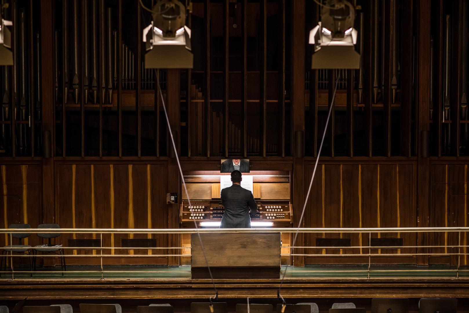 Rückansicht eines Organisten an der Orgel, aus der Ferne betrachtet.