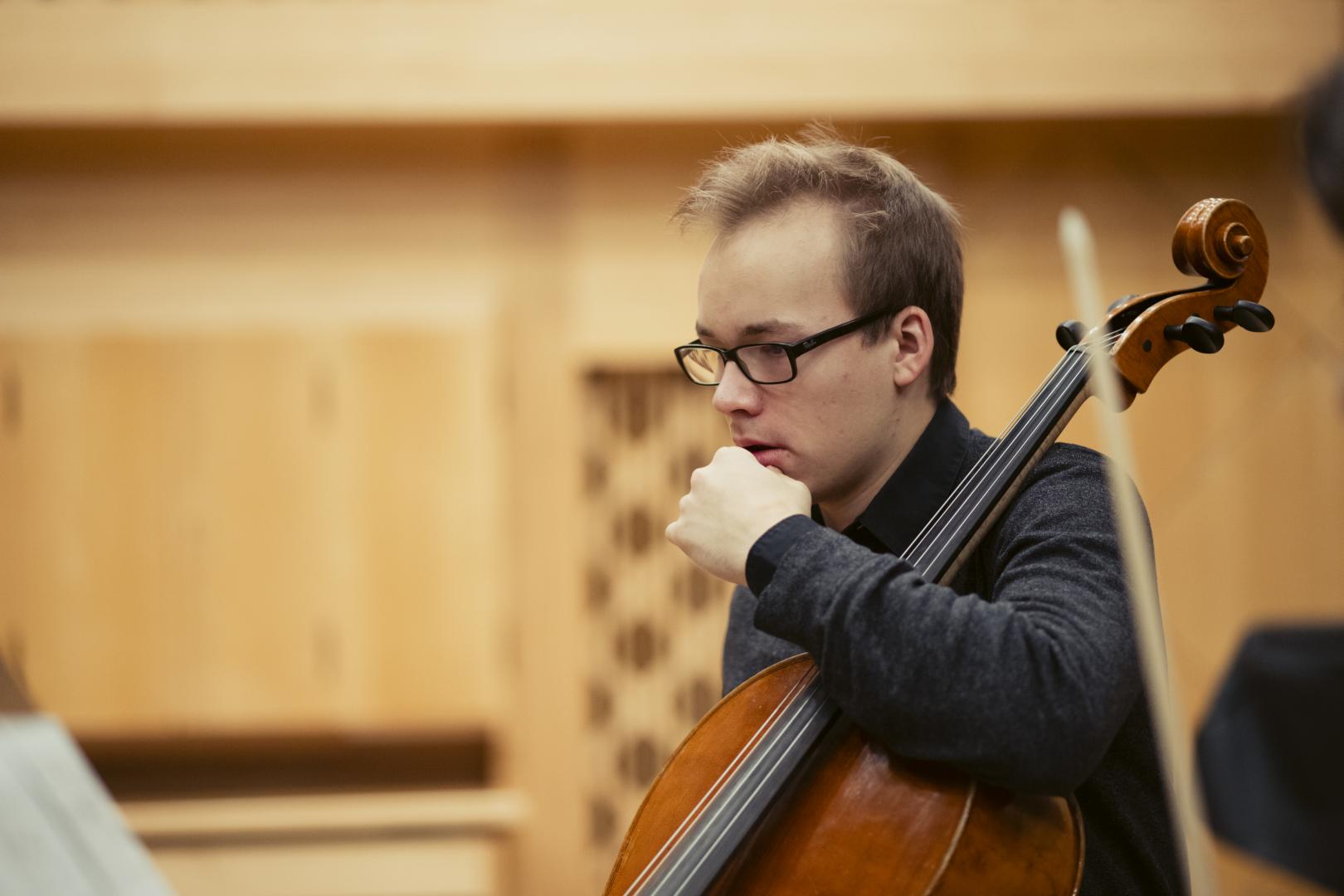 Ein Cellist mit seinem Instrument betrachtet nachdenklich die Noten vor ihm