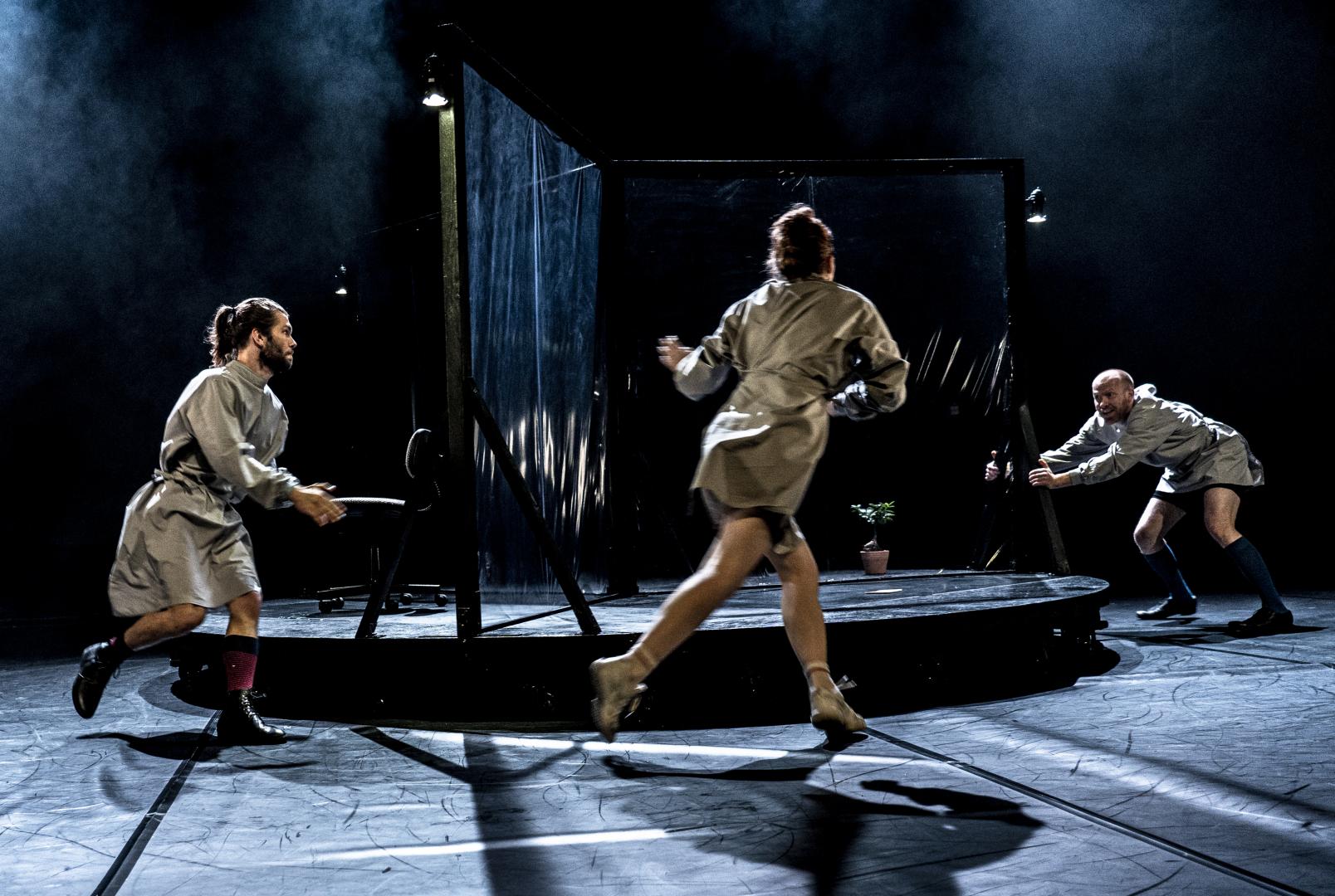 Drei Schauspielerinnen rennen im Kreis um einen drehbaren Bühnenaufbau, düsteres Licht