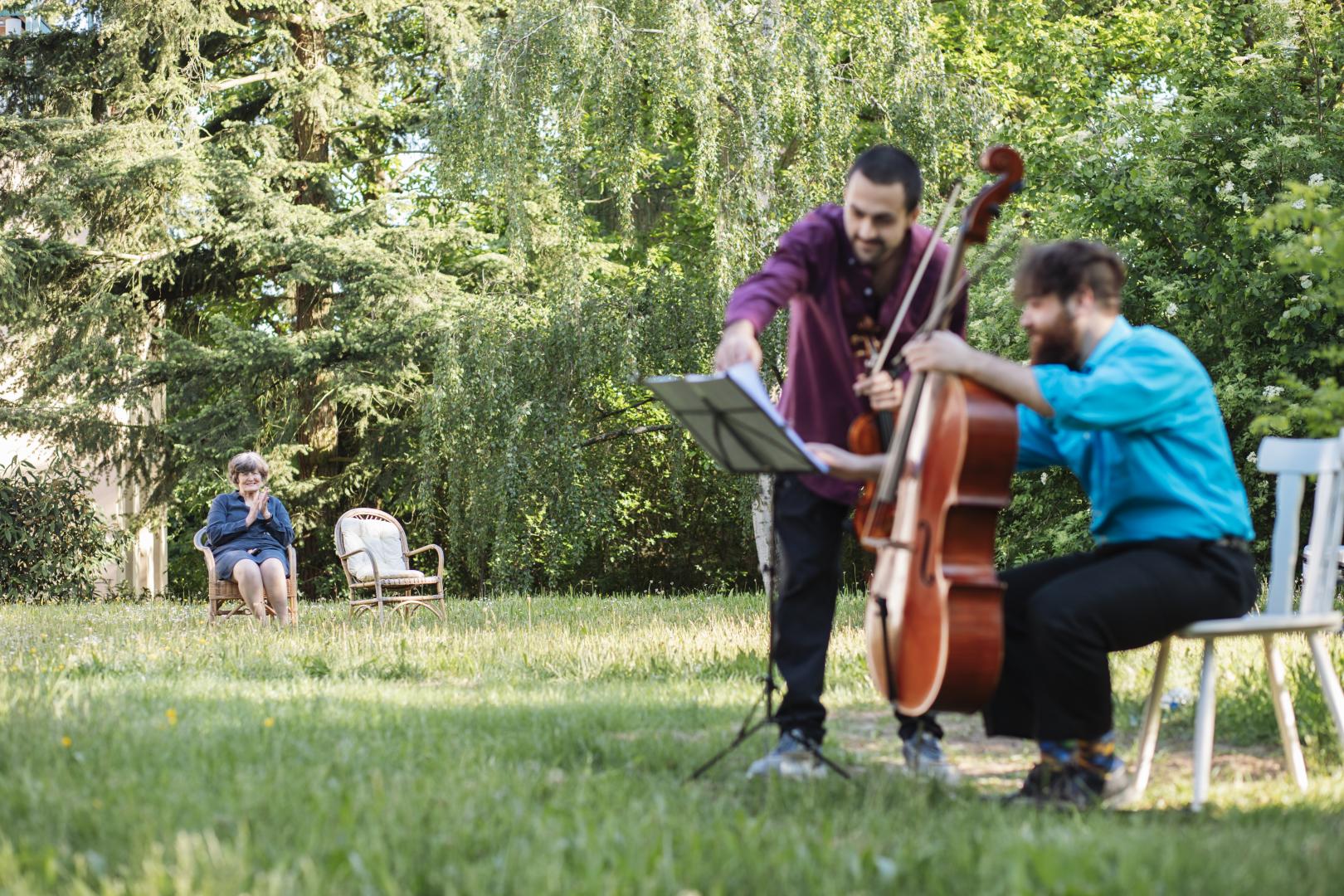 Zwei Musiker im Garten, eine Frau sitzt einige Meter weg und klatscht