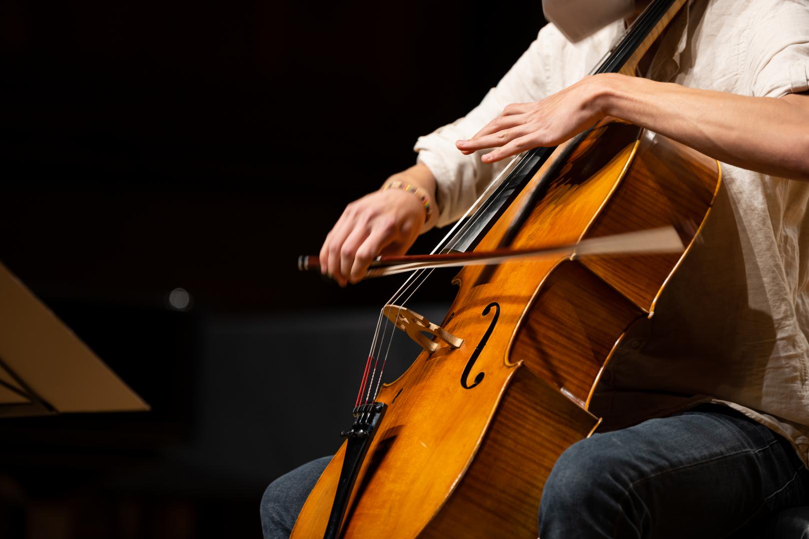 Ein Cellist spielt sein Instrument, die schnelle Bewegung des Bogens ist im Bild zu sehen
