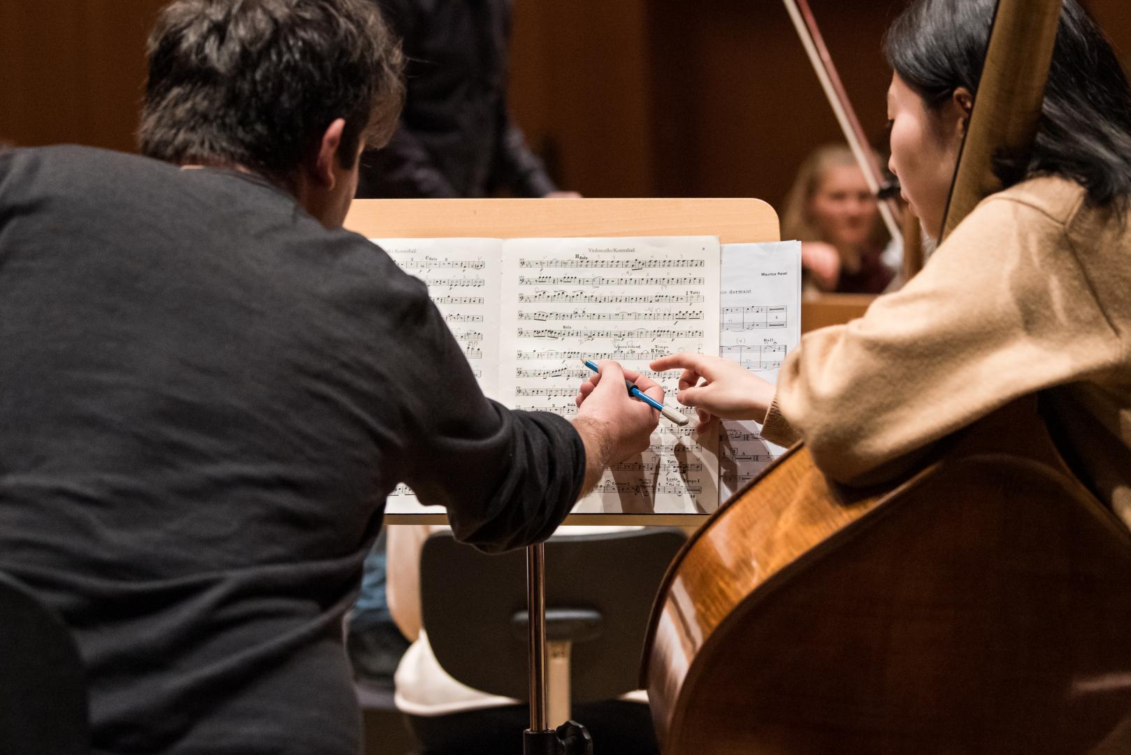 Eine Kontrabassistin und ein Kontrabassist, in der Orchesterprobe über Noten gebeugt.