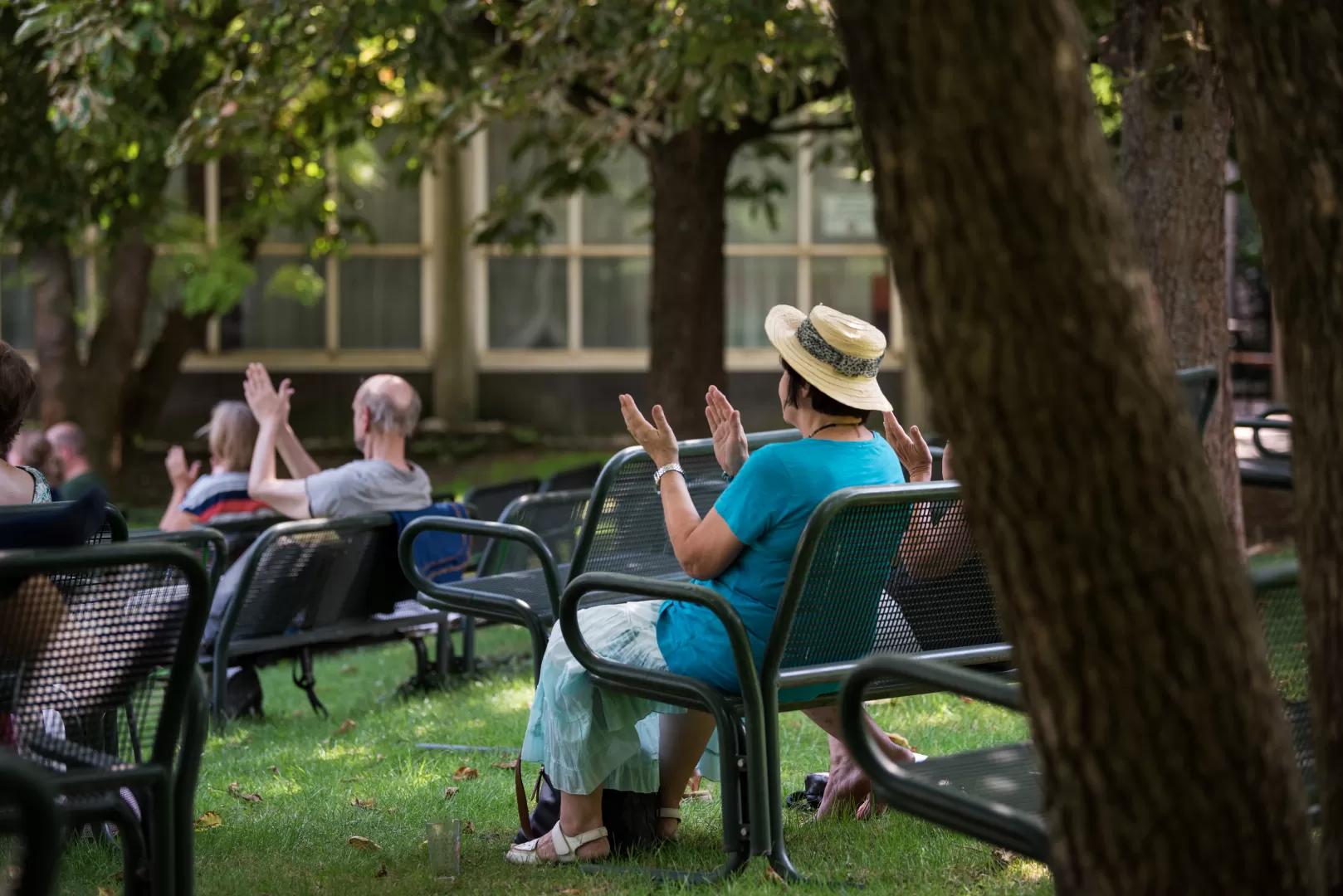 Eine Person mit Strohhut sitzt auf einer Bank und applaudiert.