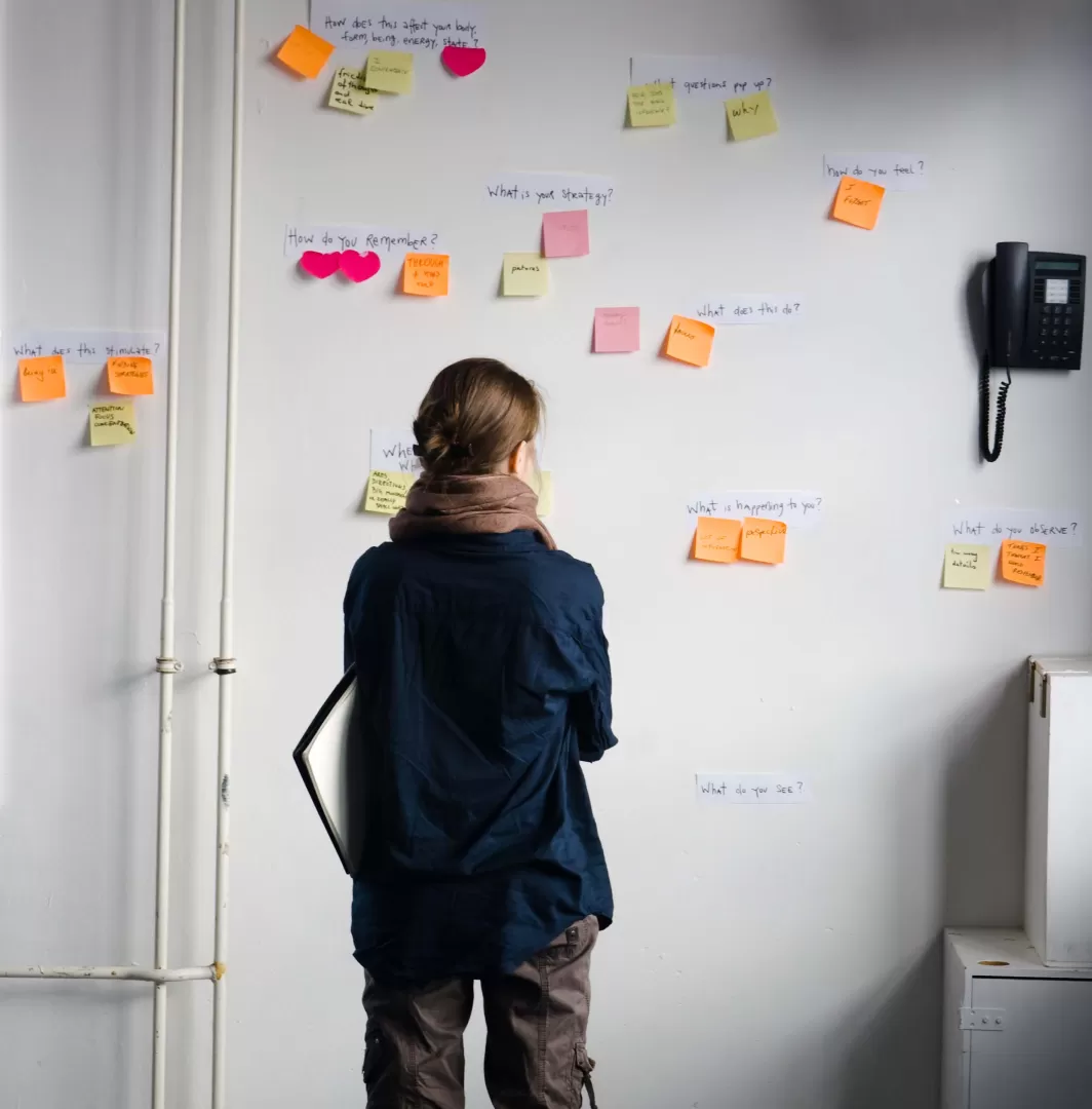Eine Frau betrachtet eine Wand, an der Post-Its mit Fragen kleben.