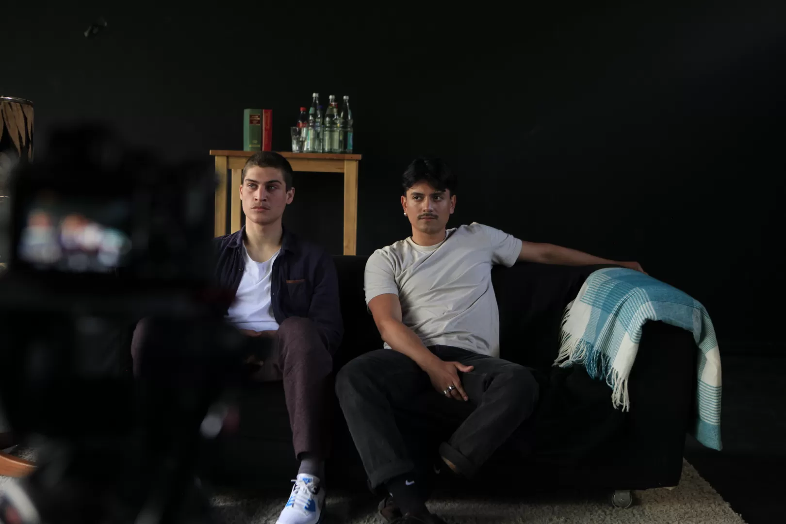 Zwei Schauspielstudierende auf schwarzem Sofa vor einer Filmkamera.