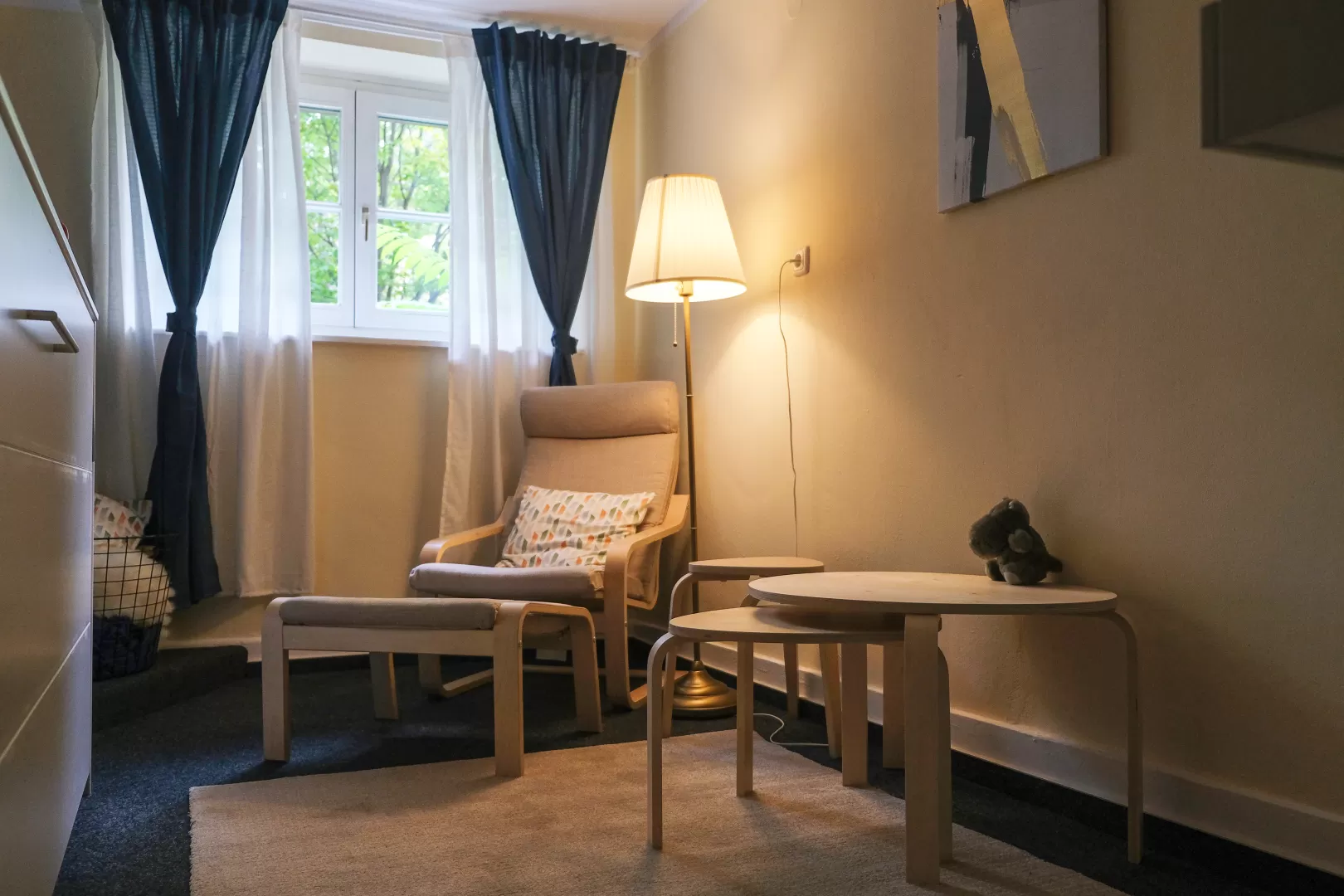 Eltern-Kind-Raum mit Sessel, Teppich und einer Stehlampe, die gemütliches Licht ausstrahlt.