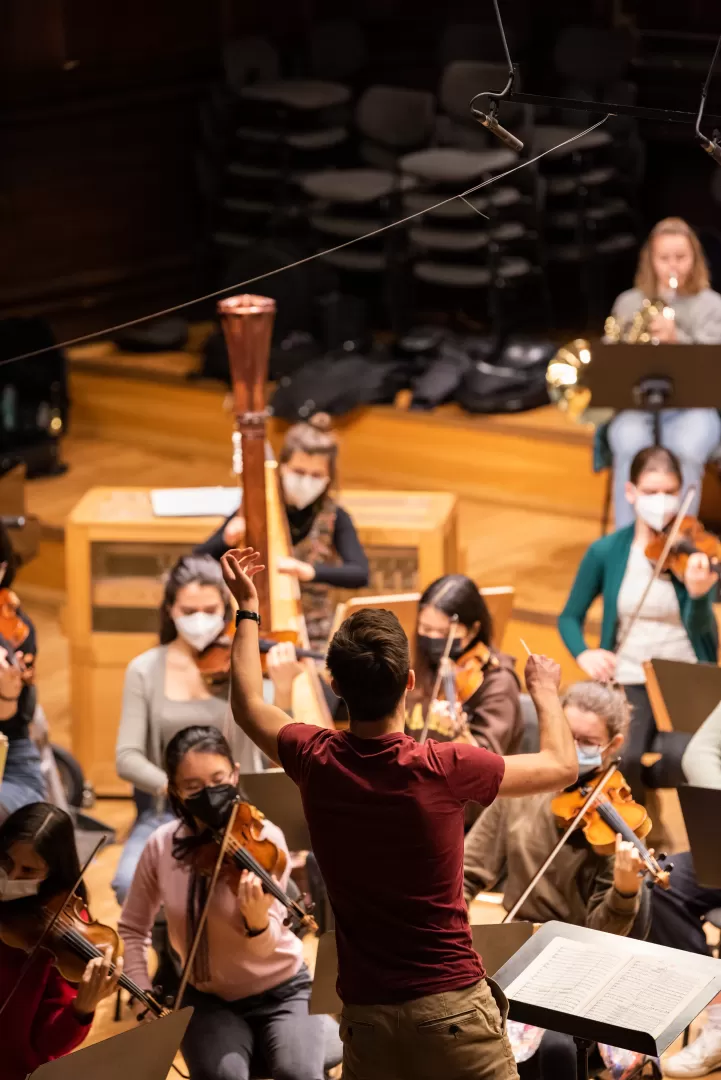 Dirigierstudent leitet ein Orchester, Hand und Taktstock erhoben.