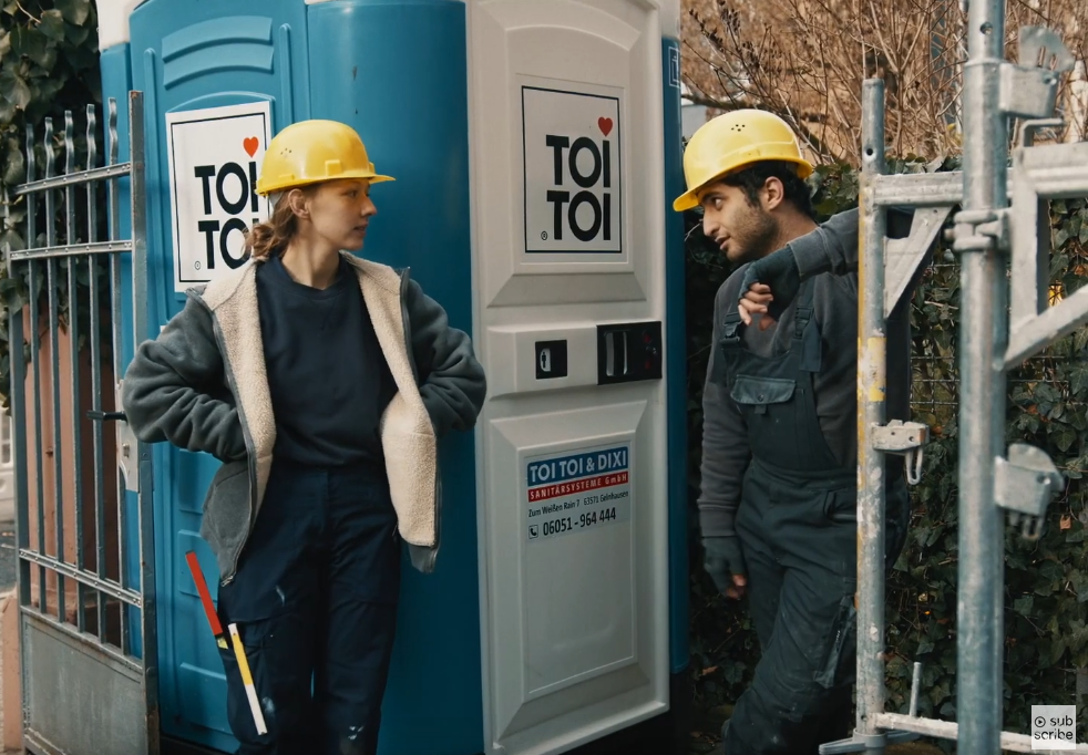 Ein Bauarbeiter und eine Bauarbeiterin stehen für einer Dixi-Toilette.