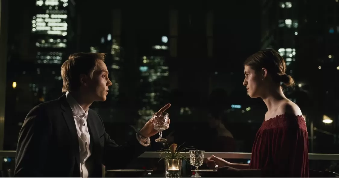 Ein Mann und eine Frau sitzen in einem Restaurante vor der Skyline Frankfurts.