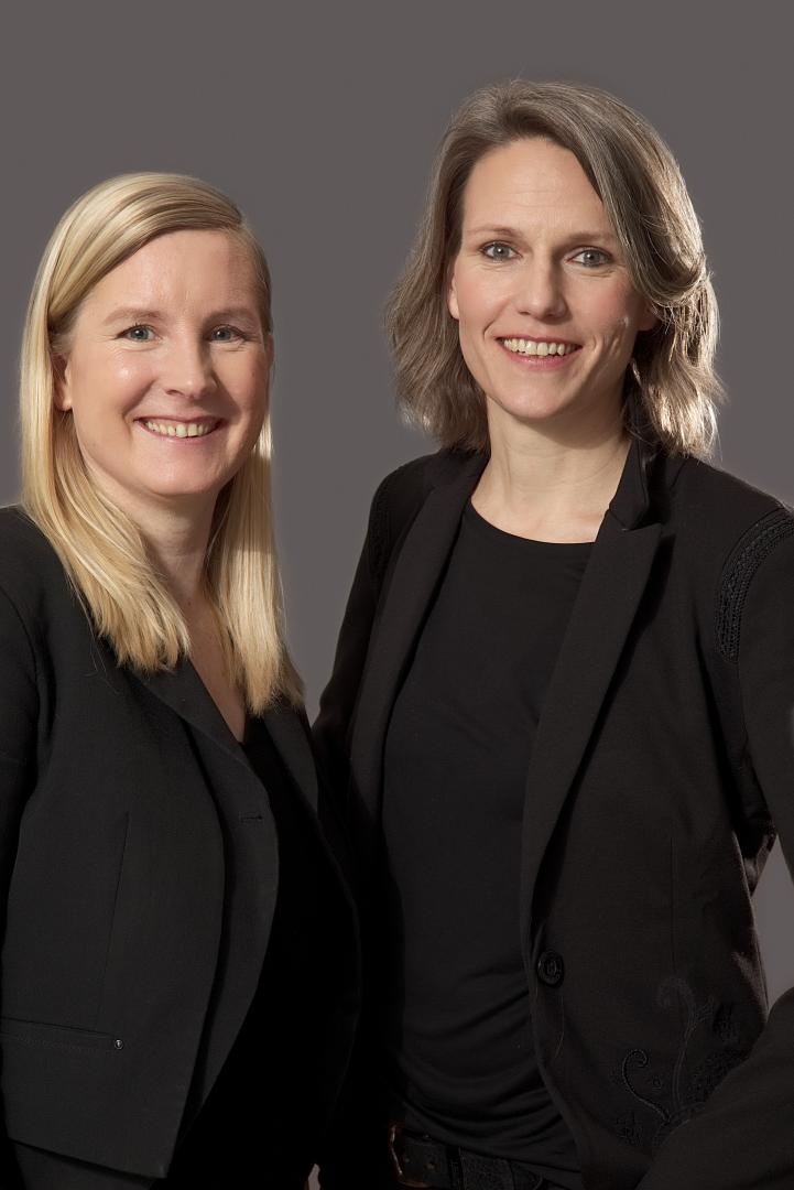 Porträtfoto von Eva Lange und Carola Unser vor einem grauen Hintergrund.
